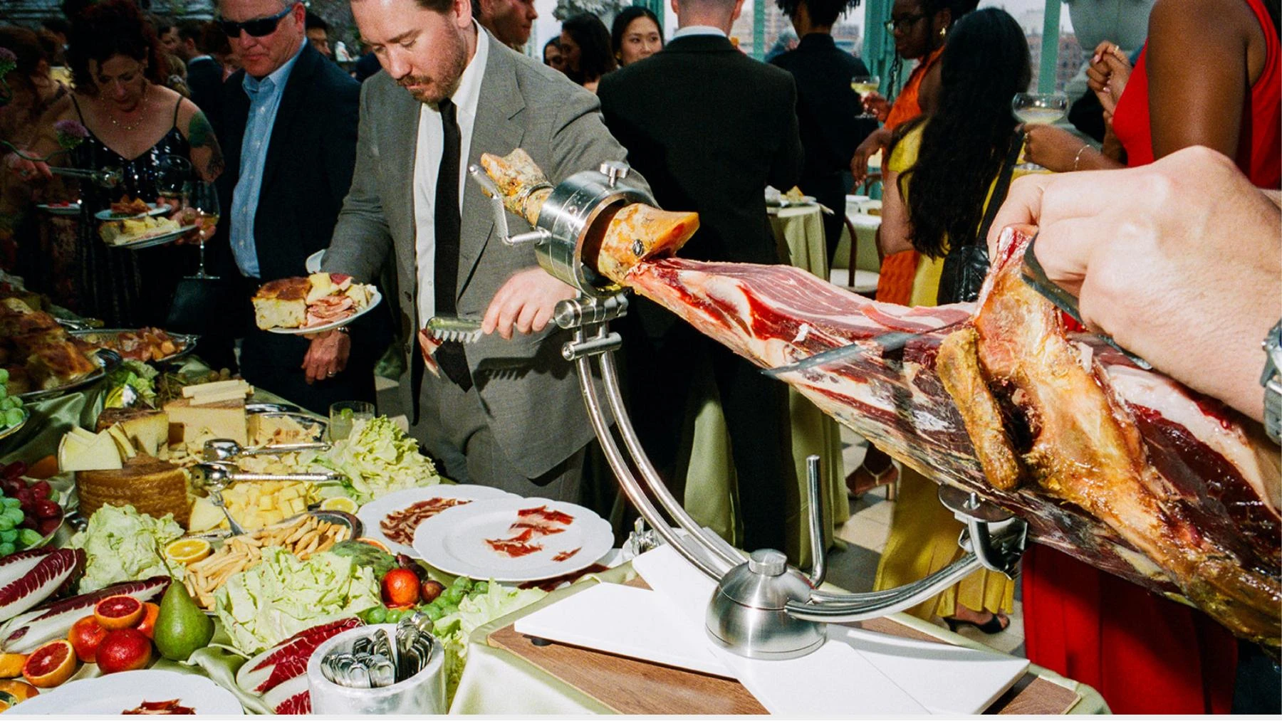Guests gathered beside hand-carved cured ham and an abundant Primo table